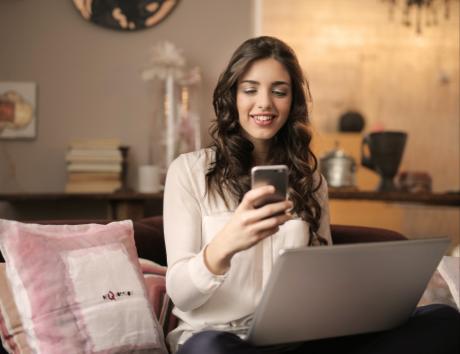 Mujer utilizando su teléfono móvil y un ordenador portátil para ilustrar la creación de un currículum en Google Docs.